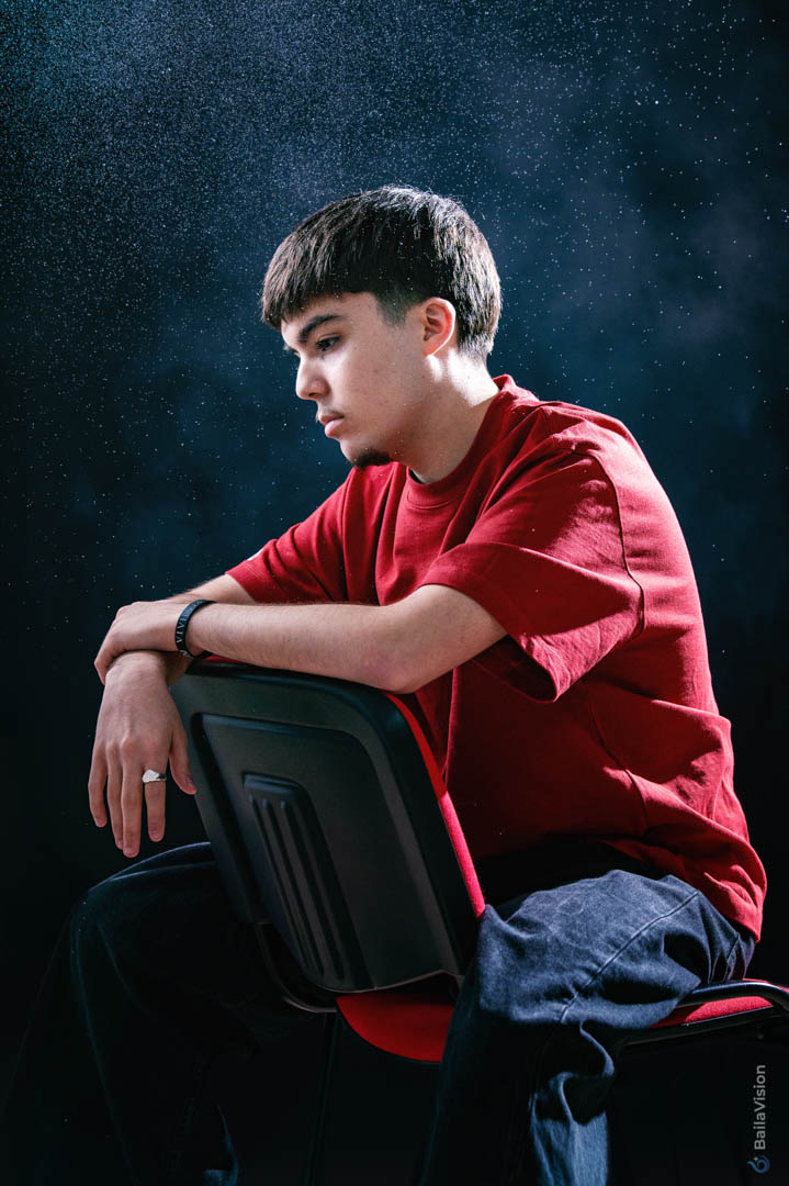Studio portrait of a male artist seated on a chair in graphic lighting